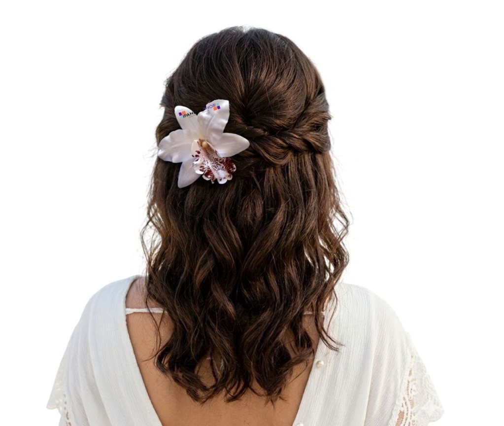Close do penteado semi-preso de noiva com cabelo castanho, adornado com uma orquídea permanente branca e marrom. Acessório floral realista para casamento na praia.
