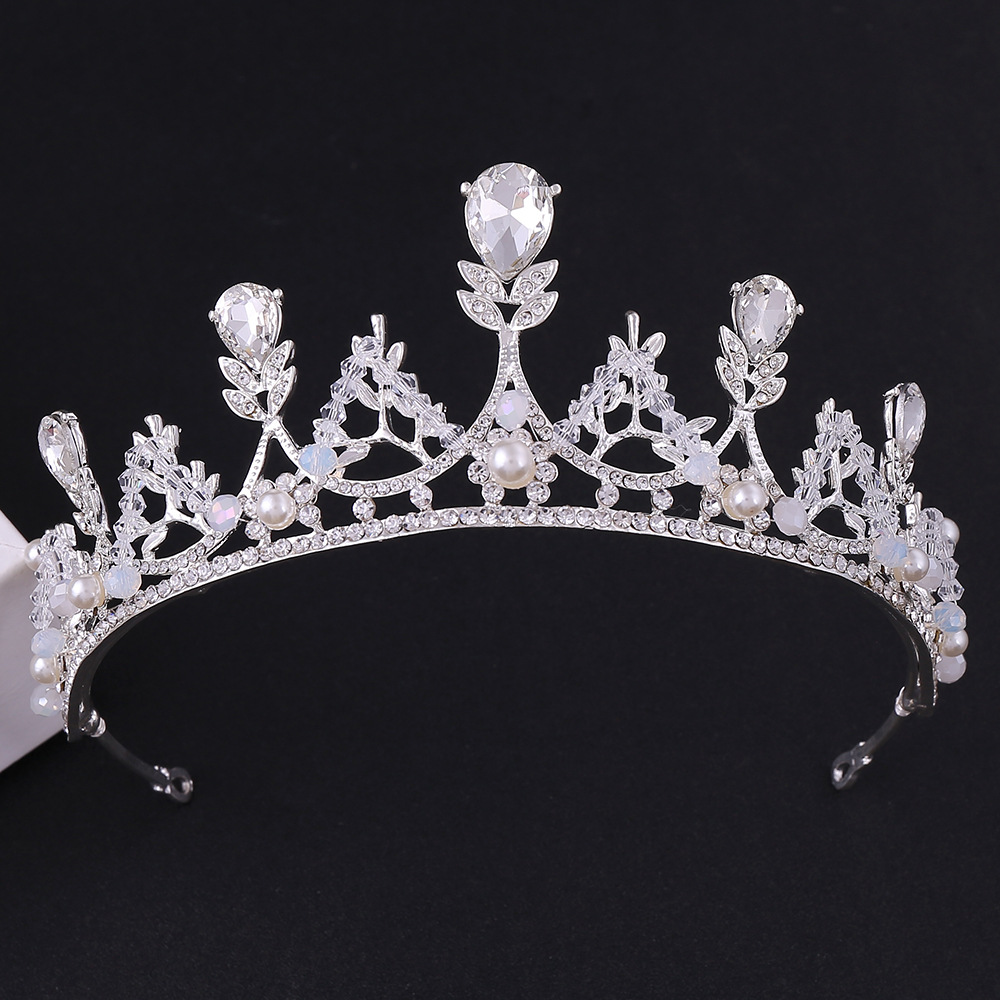 Coroa prateada de luxo para noiva ou debutante, vista de frente em fundo preto. A peça possui cristais em formato de gota e redondos, intercalados com pérolas brancas delicadas. Altura de 5,5cm.