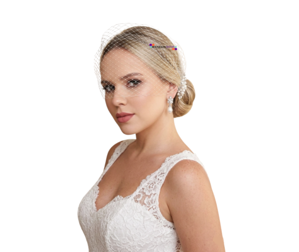 Acessório de noiva estilo voilette em tela off-white cobrindo os olhos, preso lateralmente em um coque com detalhes de pérolas, usado por noiva loira com vestido de renda branca.